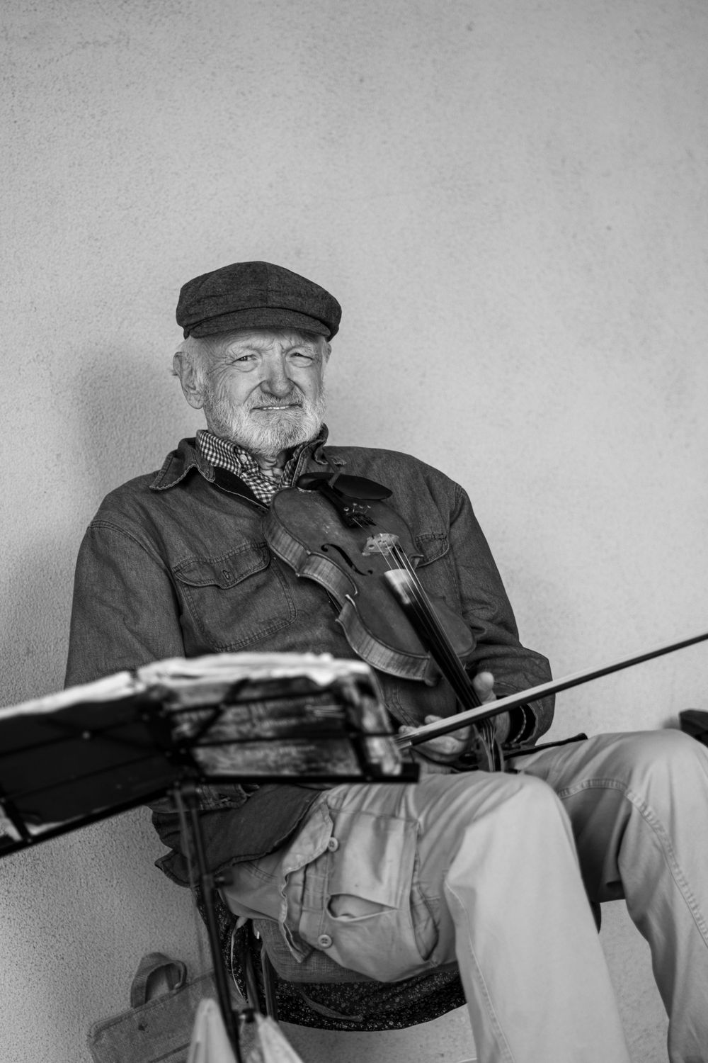 Elderly person in a cap sitting with a rifle in a black and white portrait.