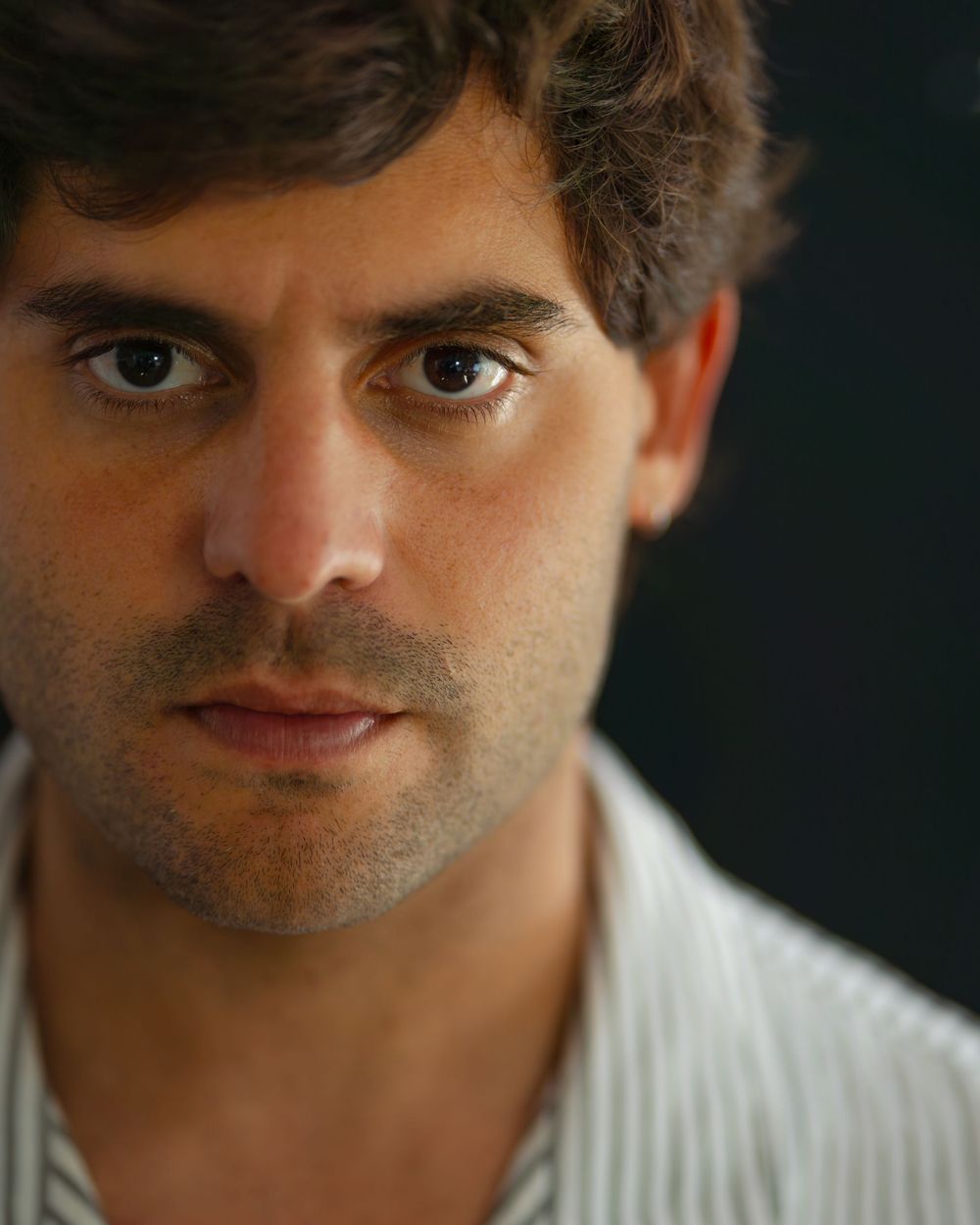 Dramatic close-up portrait with moody lighting and white collared shirt.