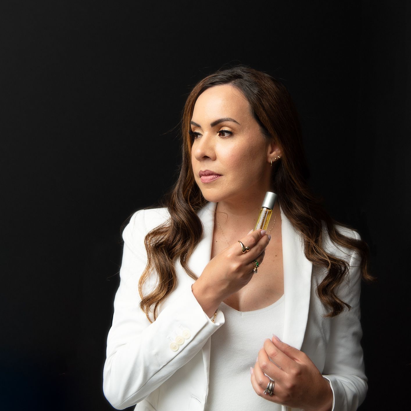 Professional woman in white blazer holding microphone against dark background.