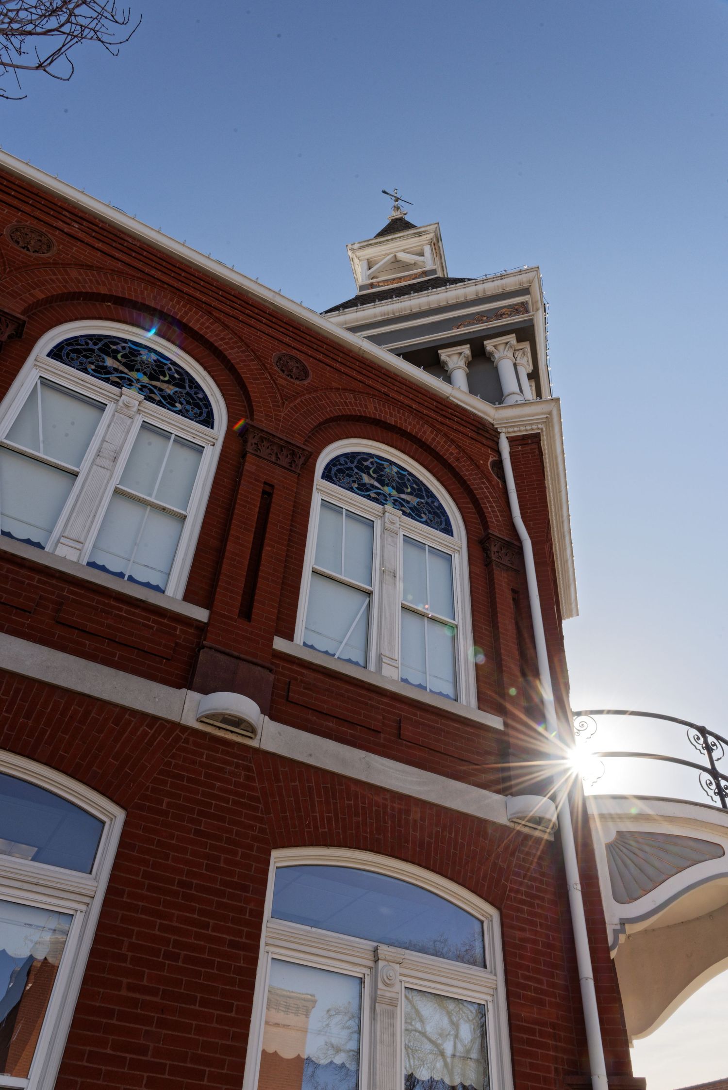 Looking up at a historic red brick building with arched windows and a clock tower against bright blue sky.