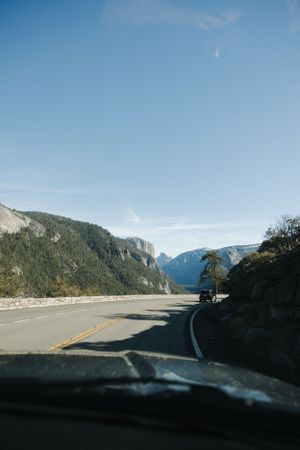 Scenic mountain highway winding through forested valley with blue skies and distant peaks, Half Dome, Yosmite.