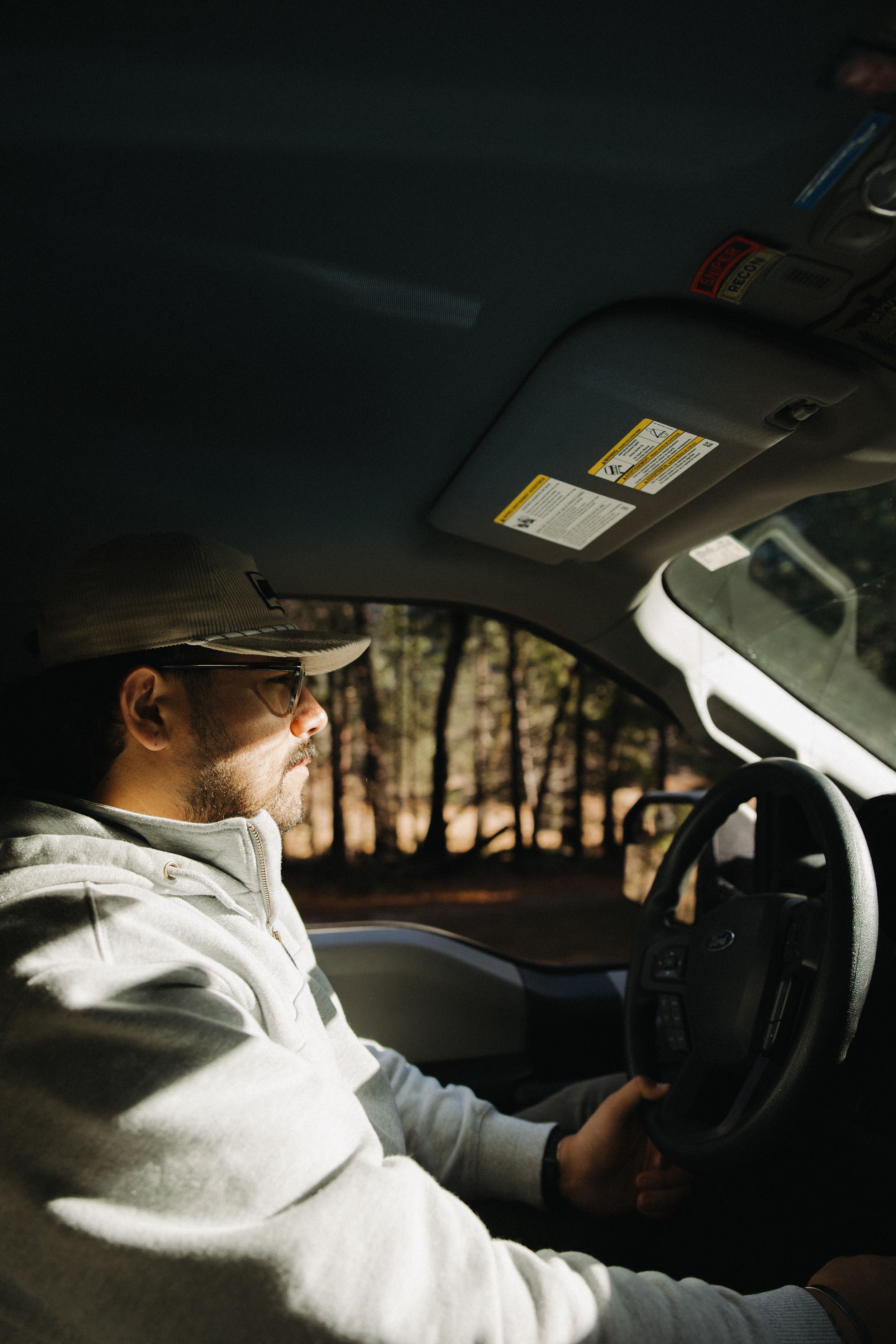Person in light colored clothing and hat driving a vehicle through a wooded area during golden hour, vintage film vibes.