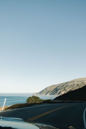 Coastal highway curves along rugged cliffs overlooking the Pacific Ocean on a clear day, Big Sur, California.