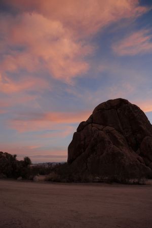 Large boulder formation silhouetted against pink and purple sunset sky in desert landscape, Indian Cove, Joshua Tree.