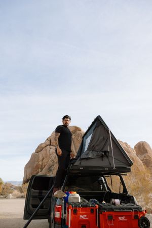 A rooftop tent setup on a vehicle with camping gear in a desert landscape with rocky formations, at Indian Cove in Joshua Tree.