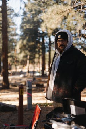Person in winter clothing stands at a campsite in a pine forest.