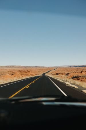 Long empty highway stretches through desert landscape under blue sky.