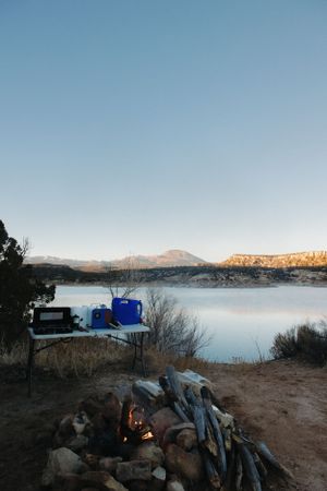 Campsite at dusk with burning campfire and camping gear overlooking a serene lake and mountain landscape, Utah.