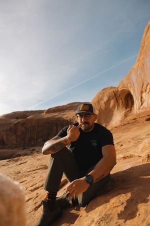 Person sitting on red sandstone rocks in outdoor desert environment, Corona Arch.