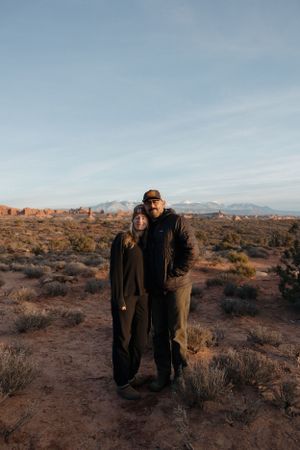 Two people standing together against desert landscape backdrop at sunset.