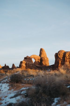 Natural rock arch formation glowing orange at sunset in desert landscape with patches of snow, Arches National Park.