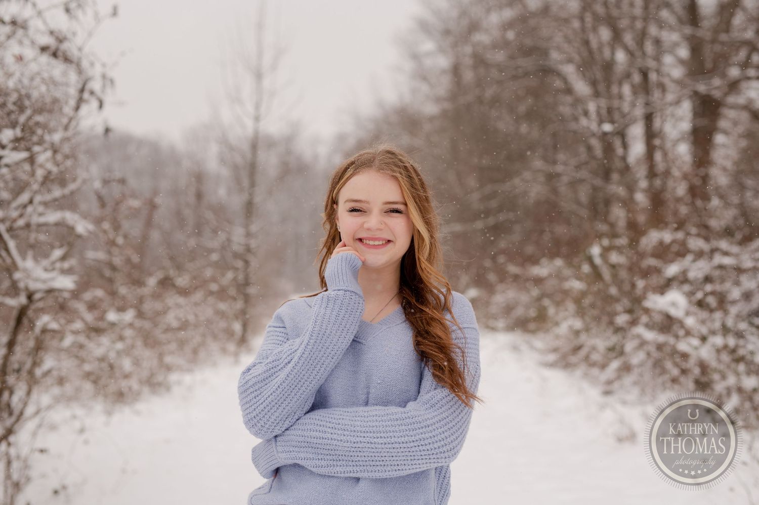 Portrait of person in blue sweater smiling against snowy winter background.