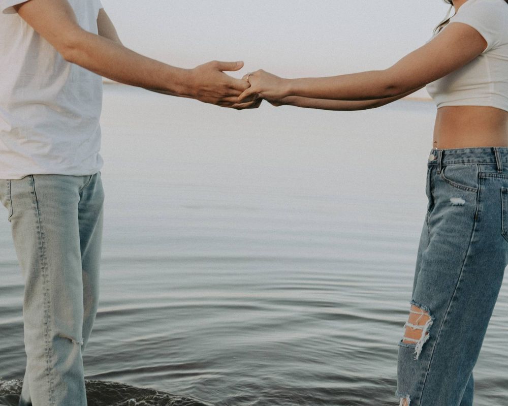 Two people holding hands against serene waterscape background.