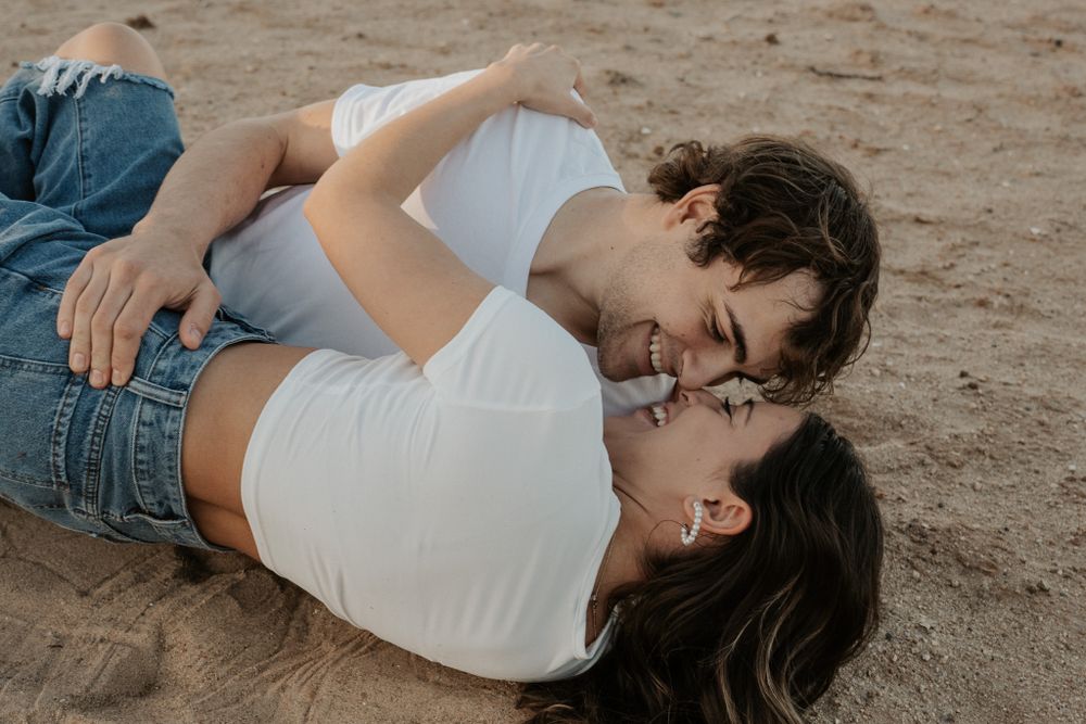 Couple lying on sandy beach sharing intimate moment during photoshoot.