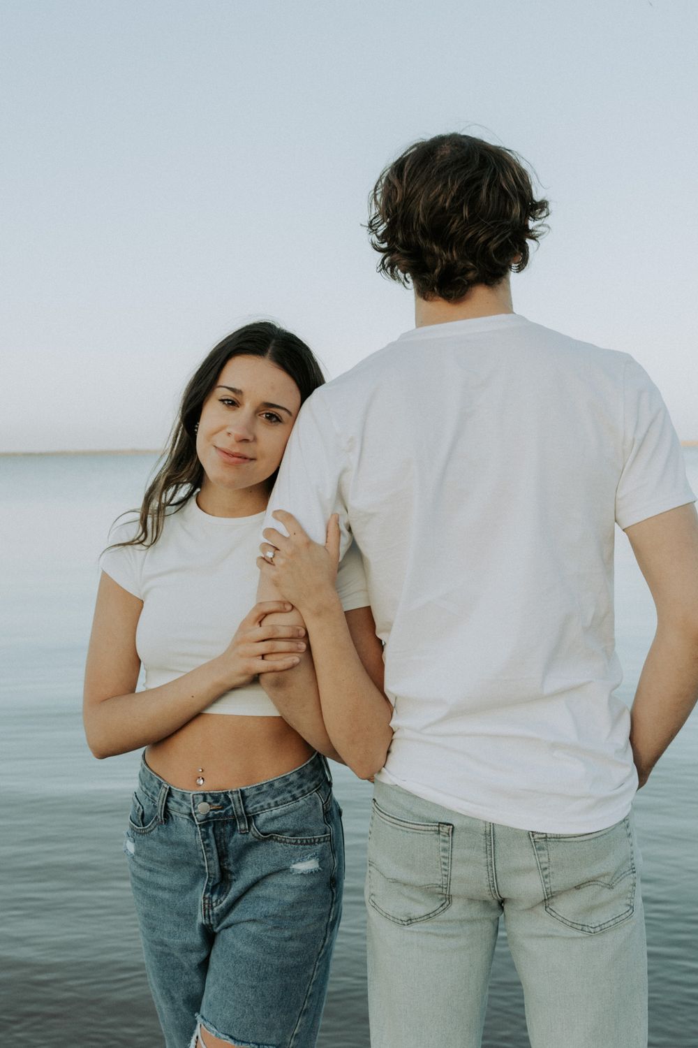 Couple in matching white t-shirts and jeans pose together by the waterfront.