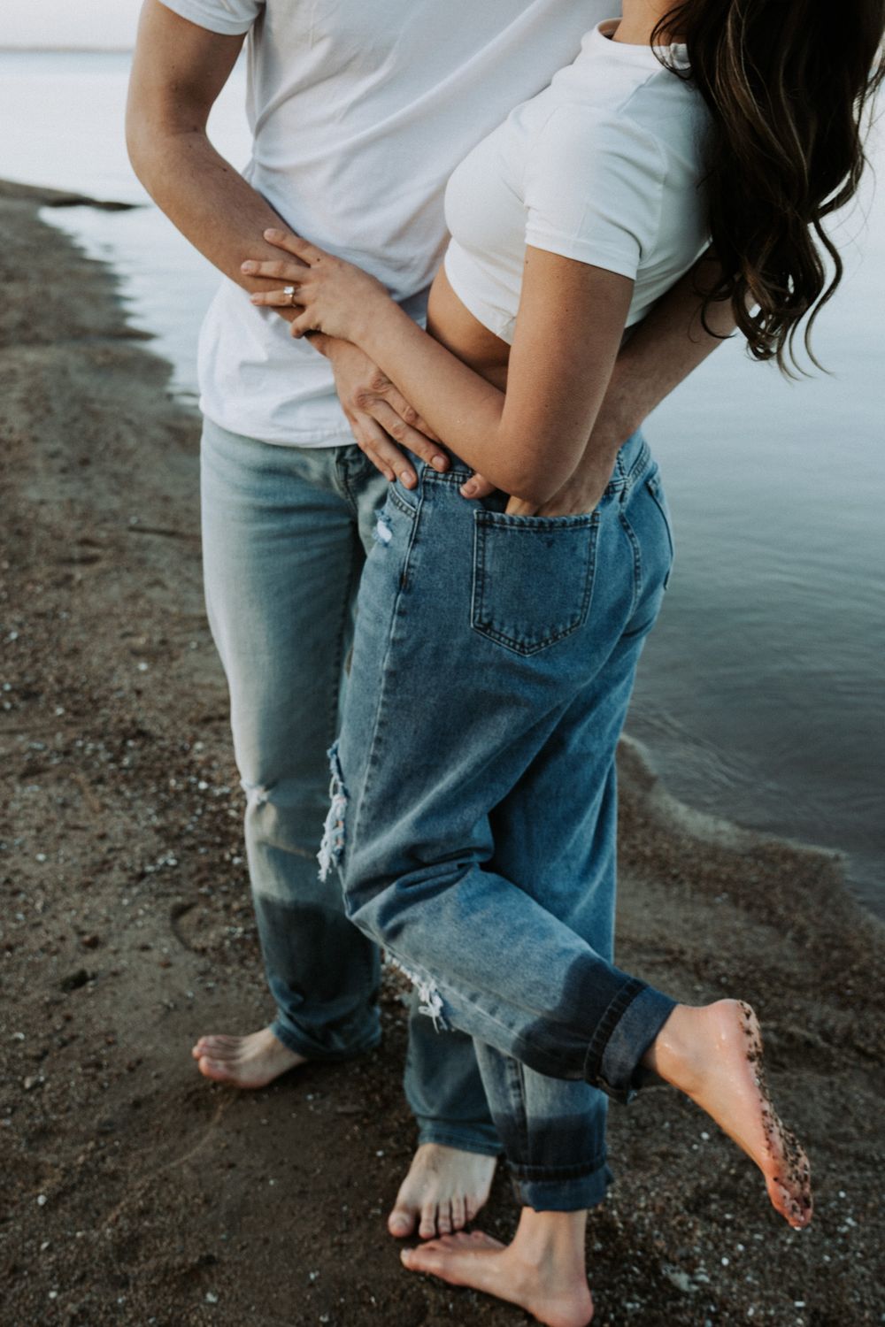 Close-up of couple's legs and bare feet as they embrace by the water's edge.