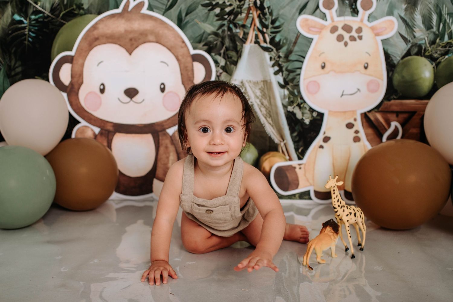 Safari nursery photo setup featuring large monkey and giraffe decorations with brown and sage green balloons.