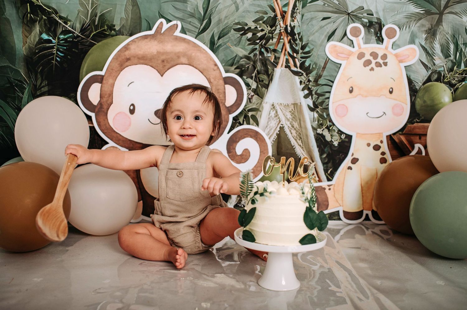 Whimsical safari-themed setup with monkey cutout, white cake stand, and brown and green balloon decor.
