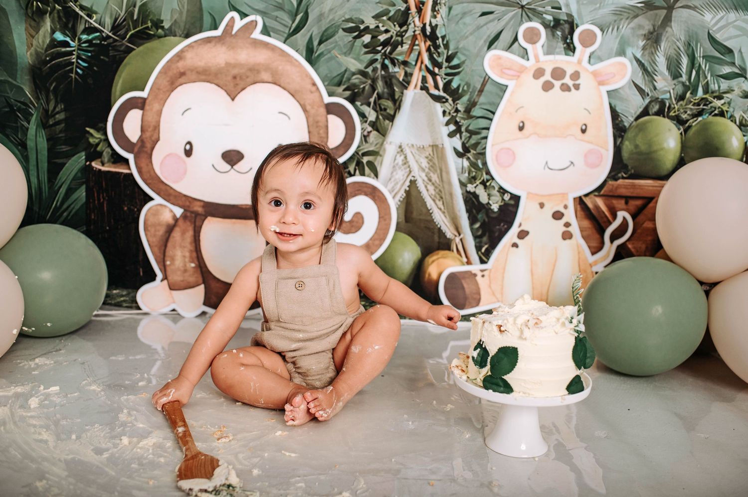 Safari nursery scene with large monkey and giraffe cutouts, white teepee, and sage green balloon decor.