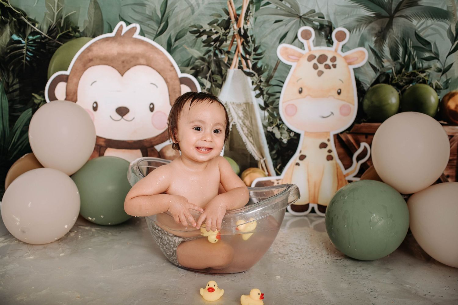 Safari-themed photo setup with clear bowl prop, monkey and giraffe cutouts, and green balloon arrangement.