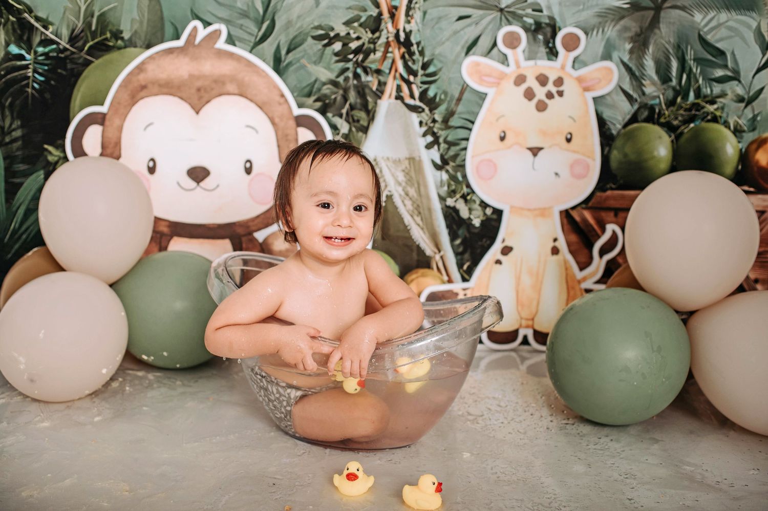 Jungle nursery scene with cartoon animal cutouts, clear bowl prop, and earth-toned balloon decorations.