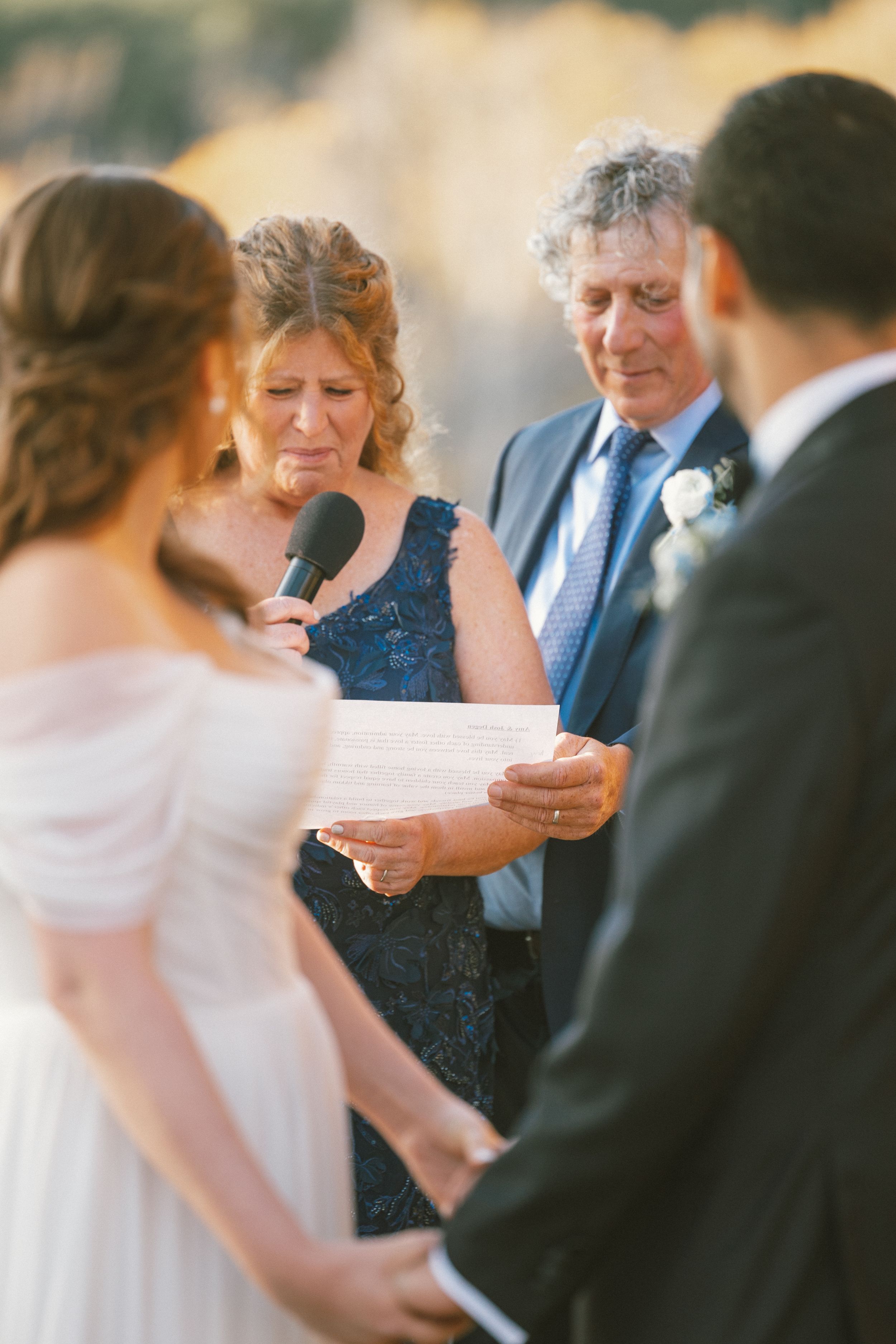 Wedding ceremony guests gather outdoors in formal attire during golden hour.