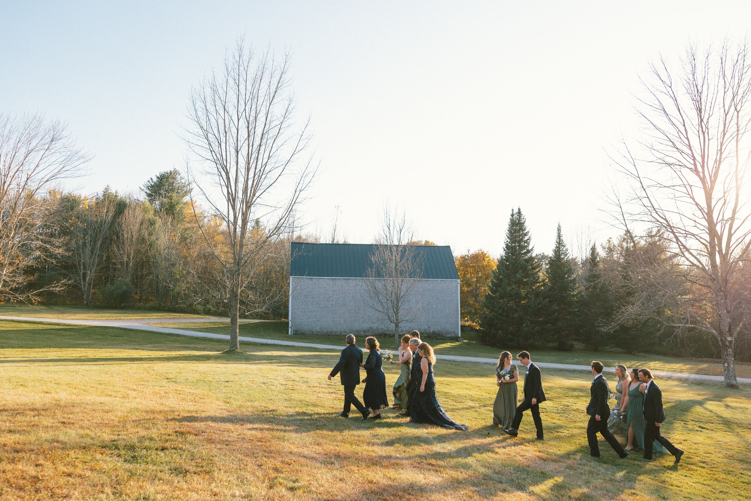 Wedding guests walking across a grassy field during golden hour.