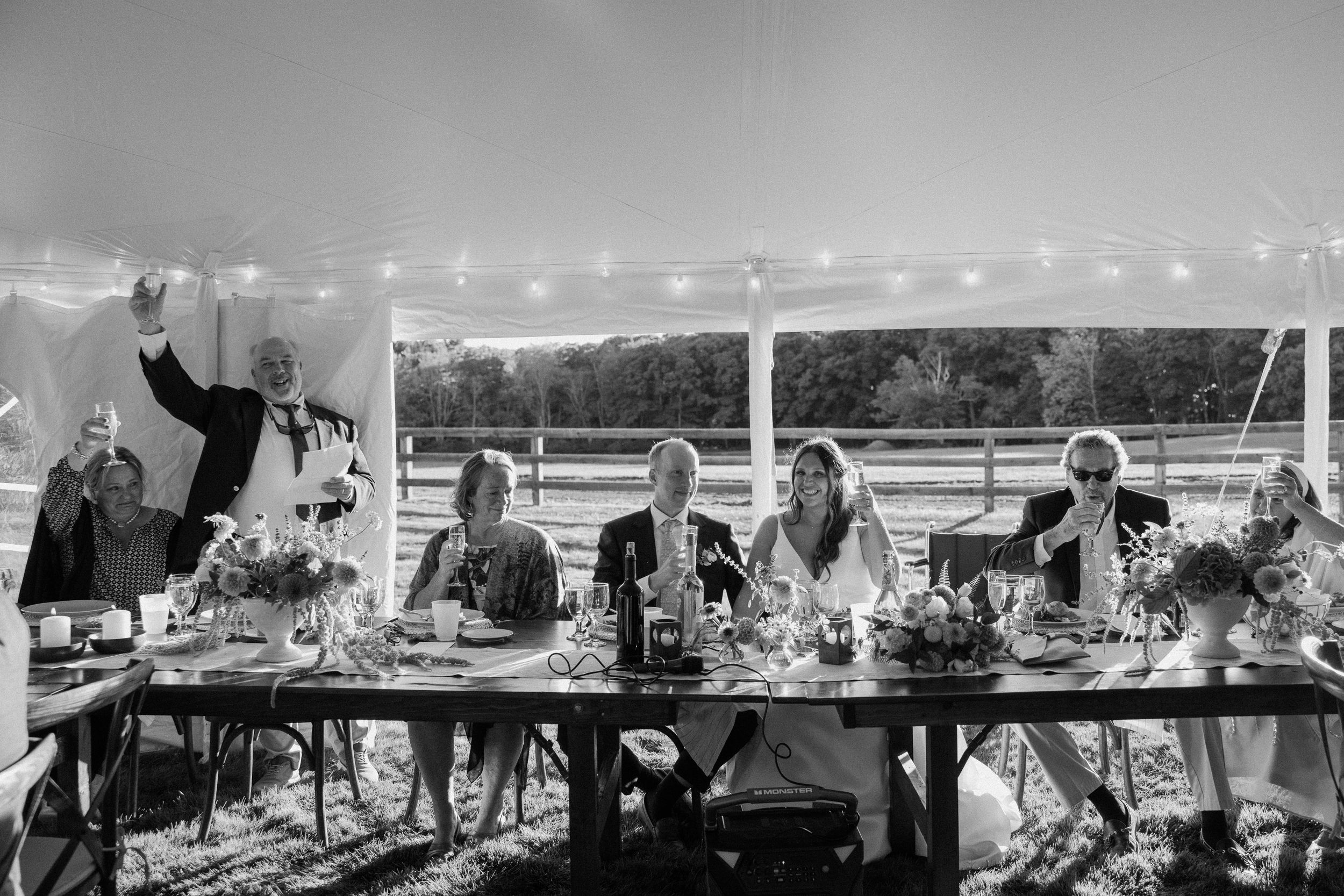 Black and white panorama of wedding guests mingling at an outdoor reception.
