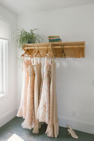 Light colored wedding dresses hang on wooden racks in a bright white room.