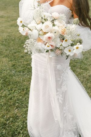 A delicate white and blush floral wedding bouquet with roses and greenery.
