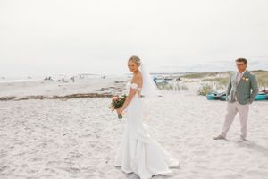 Couple walking along a scenic beach shoreline at sunset with elegant wedding attire.