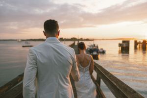 Guests gather on a waterfront deck during golden hour at a coastal wedding celebration.