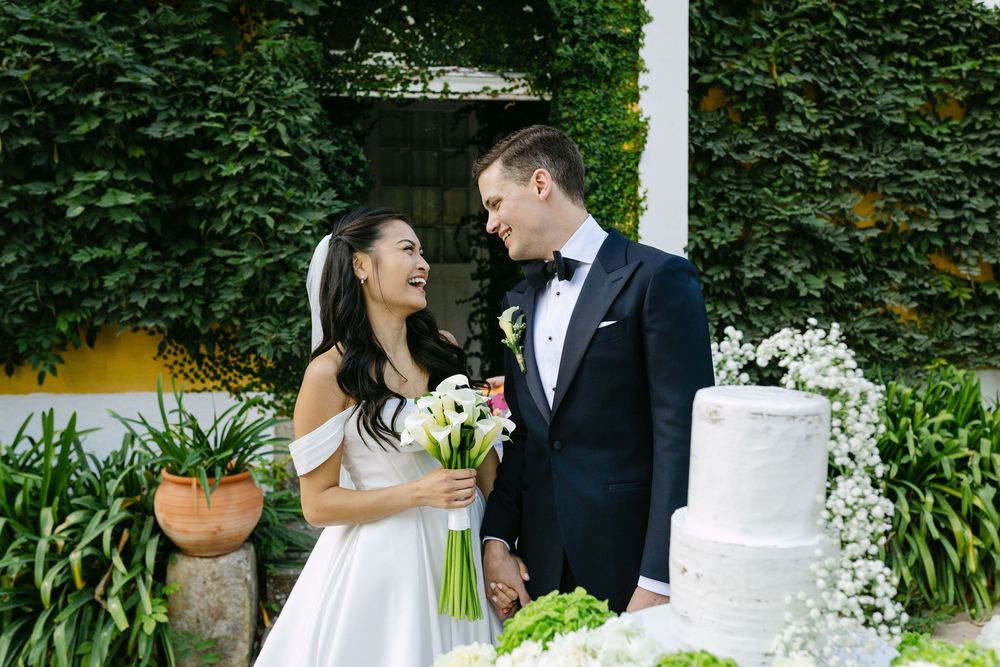 A romantic wedding couple shares sweet moments together in a lush garden setting with a white wedding cake.