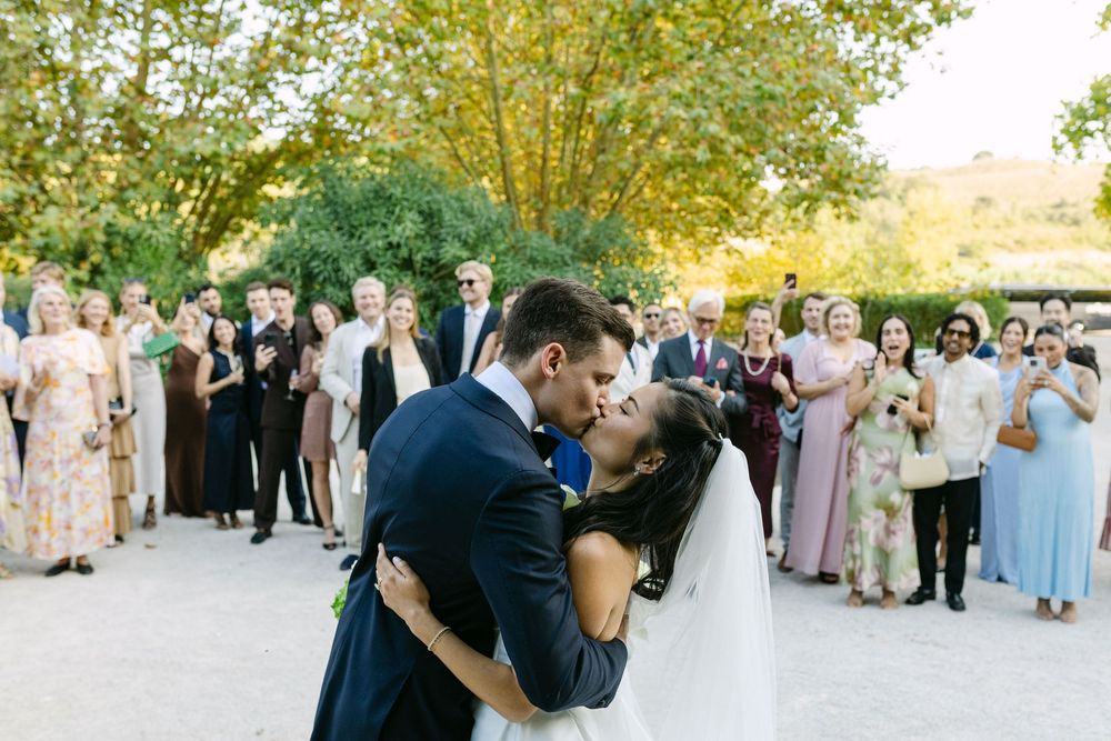 Bride and groom kissing during outdoor wedding ceremony with guests applauding in Lisbon Portugal