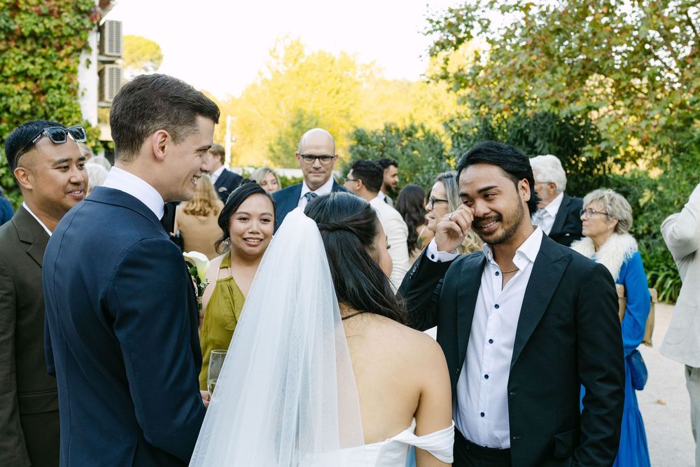 Wedding guests share joyful laughter during an outdoor celebration in a garden setting at sunset.