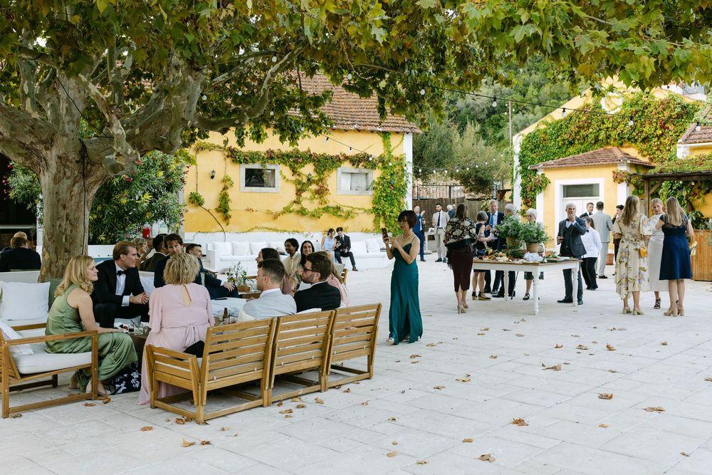 People gather at an outdoor venue is Lisbon with wooden benches and trees creating a natural, shaded environment.