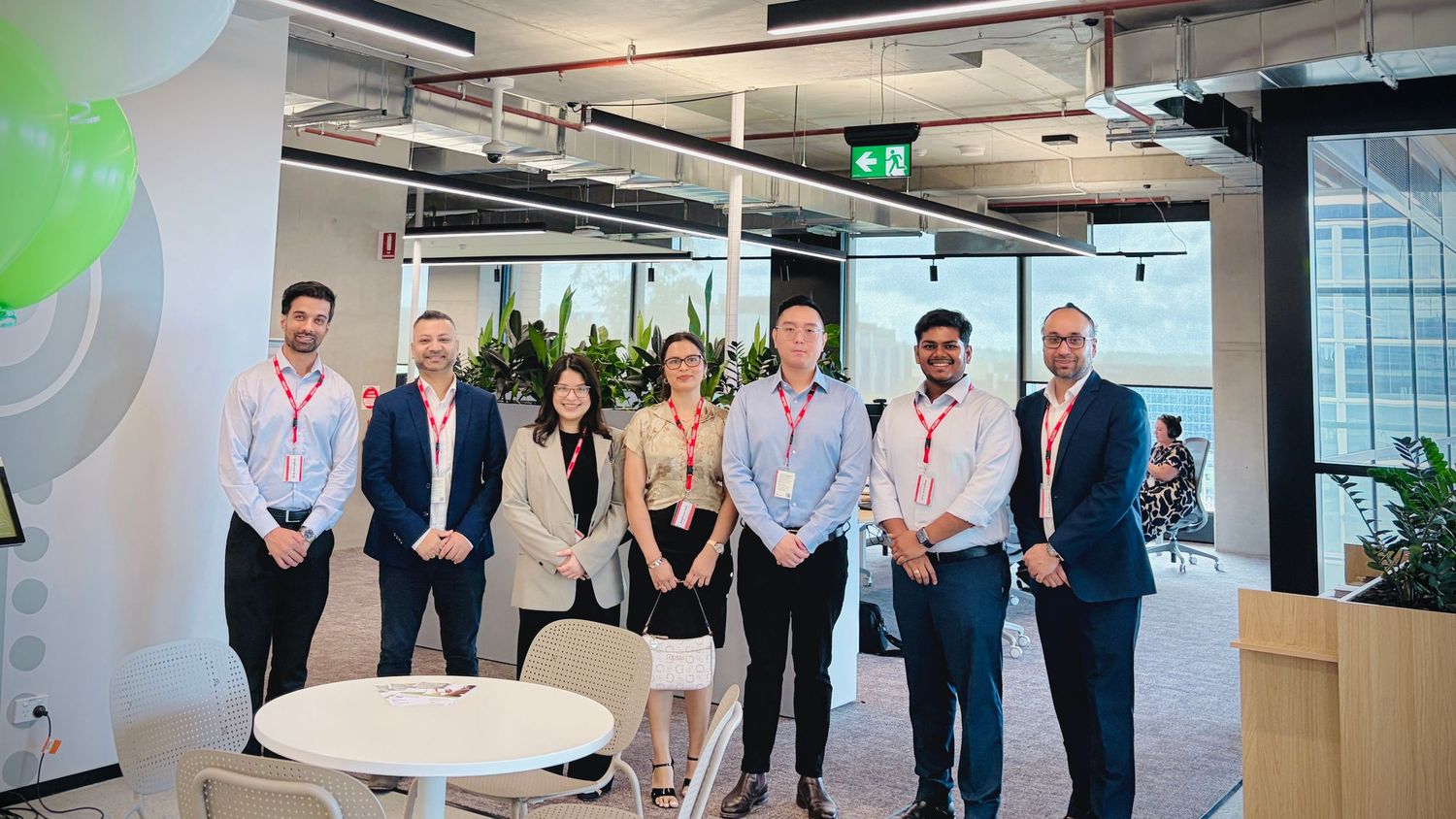 Group of seven professionals in business attire posing together in a modern office space.