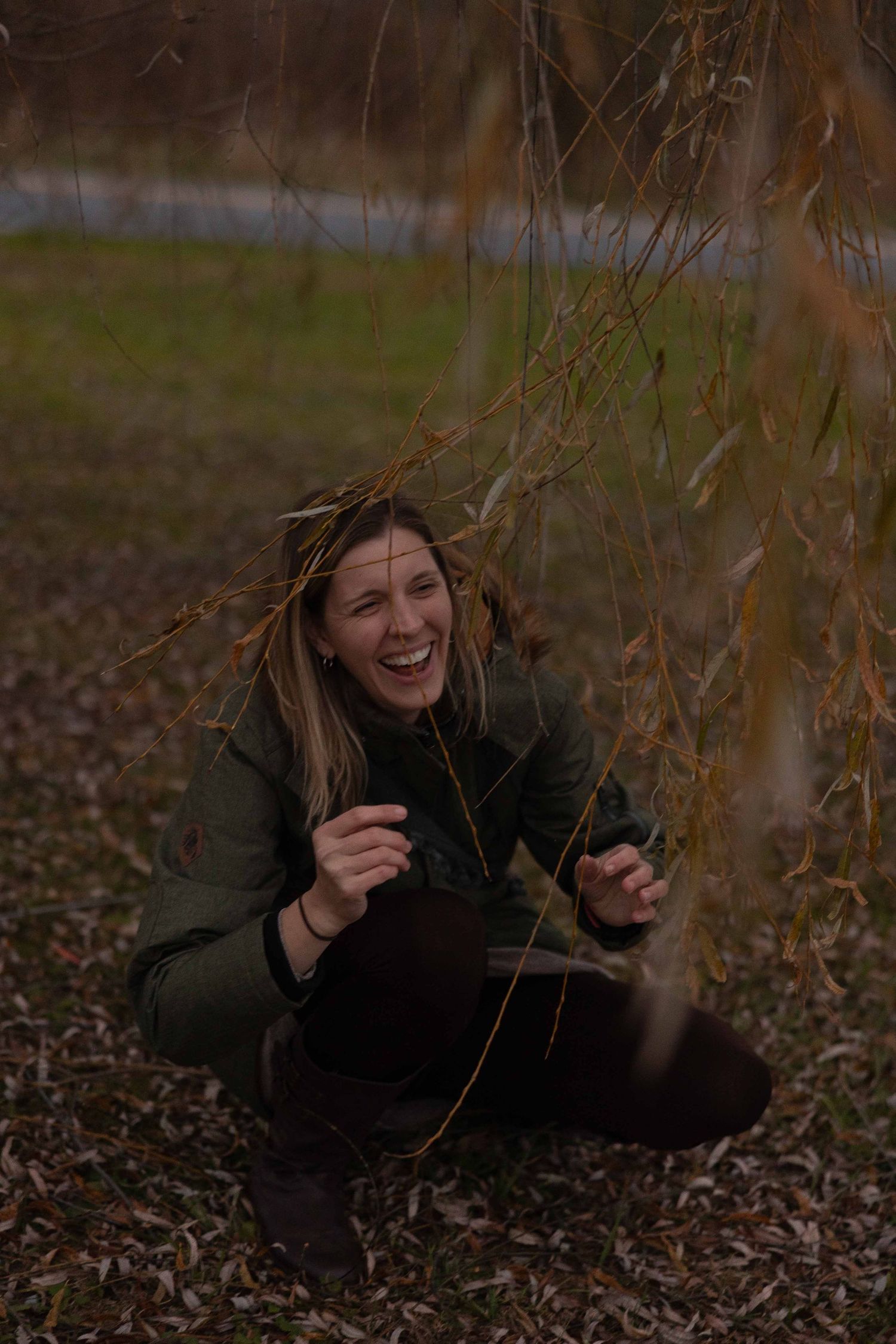 Person in dark clothing lies on autumn ground covered with fallen leaves while laughing and gesturing playfully.