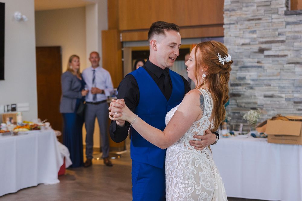 Couple in blue and white attire dance together at an elegant venue with stone walls and warm lighting.
