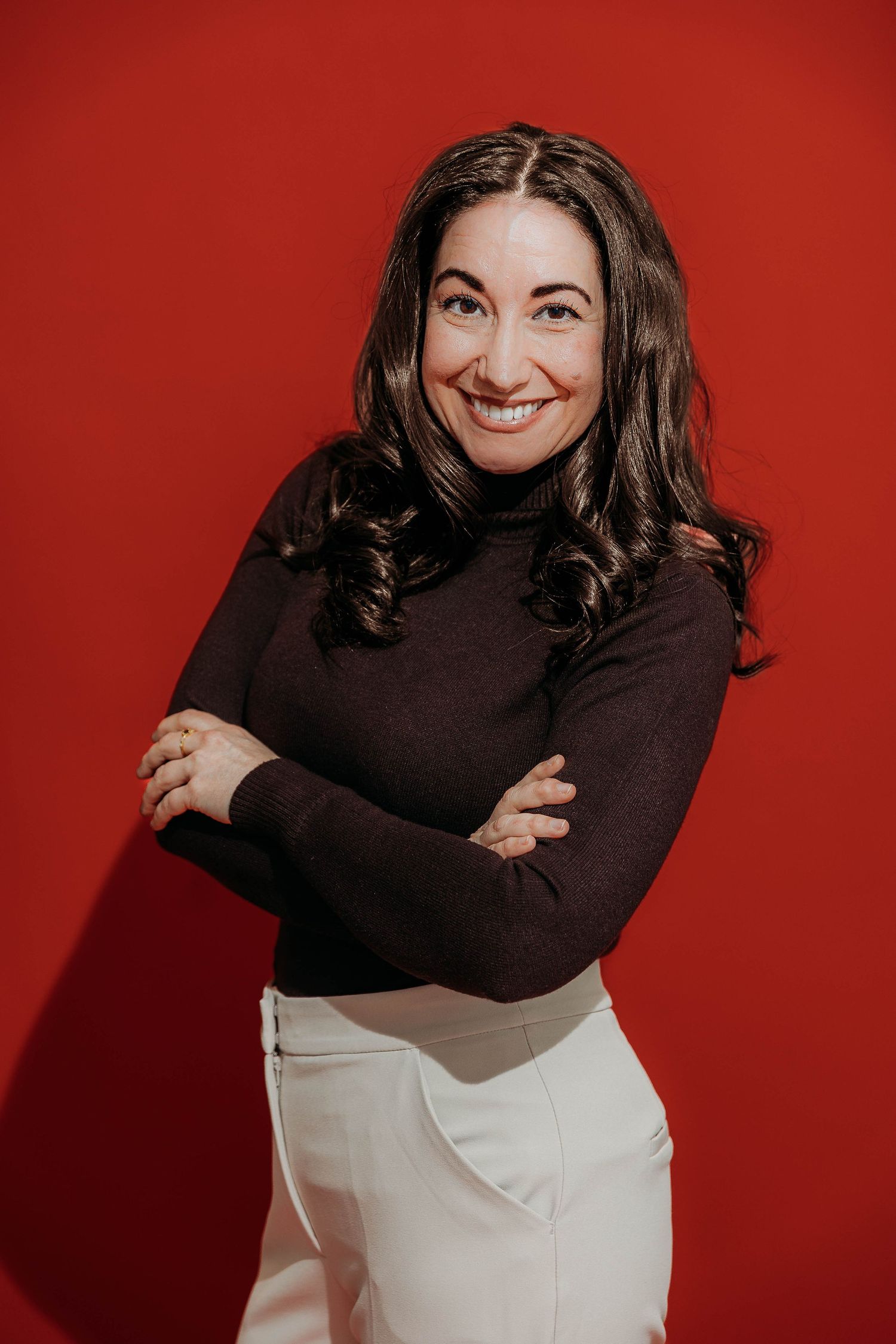 A person in a black turtleneck and white pants poses playfully against a red background in a photo series.
