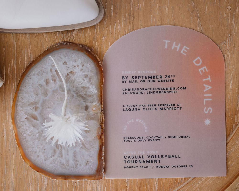 Elegant arched acrylic wedding details card with rose gold design displayed on wooden surface.