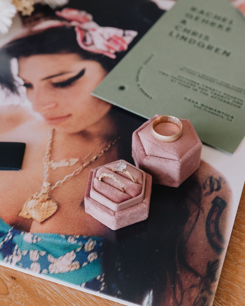 Wedding rings in pink velvet ring boxes displayed on magazine with green wedding invitation.