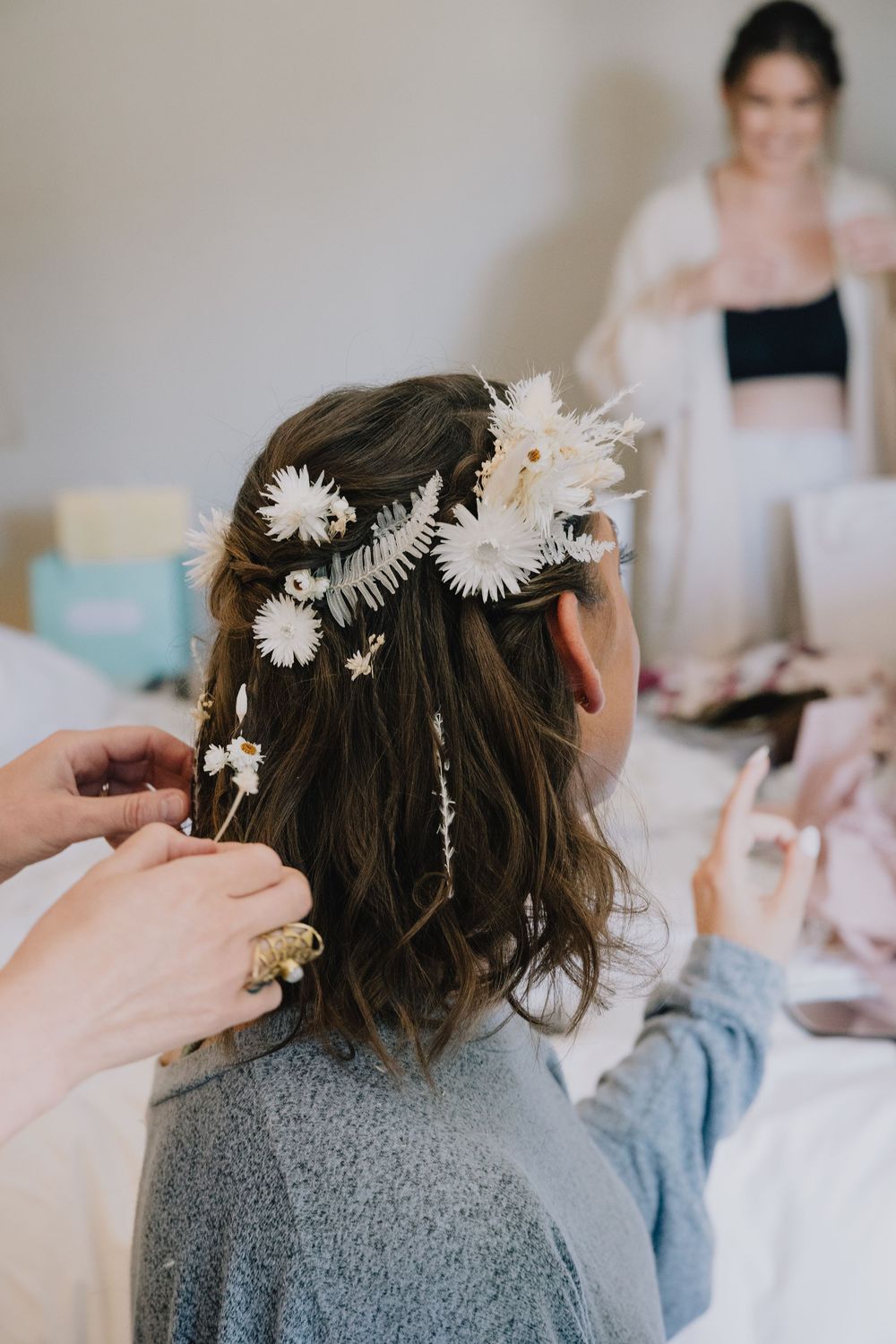 Florist arranging white daisy flower crown in brides hair during wedding preparations.