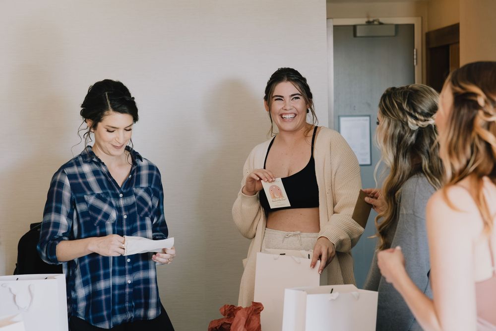 Bridesmaids laughing and opening gifts in hotel room during pre-wedding getting ready celebration.