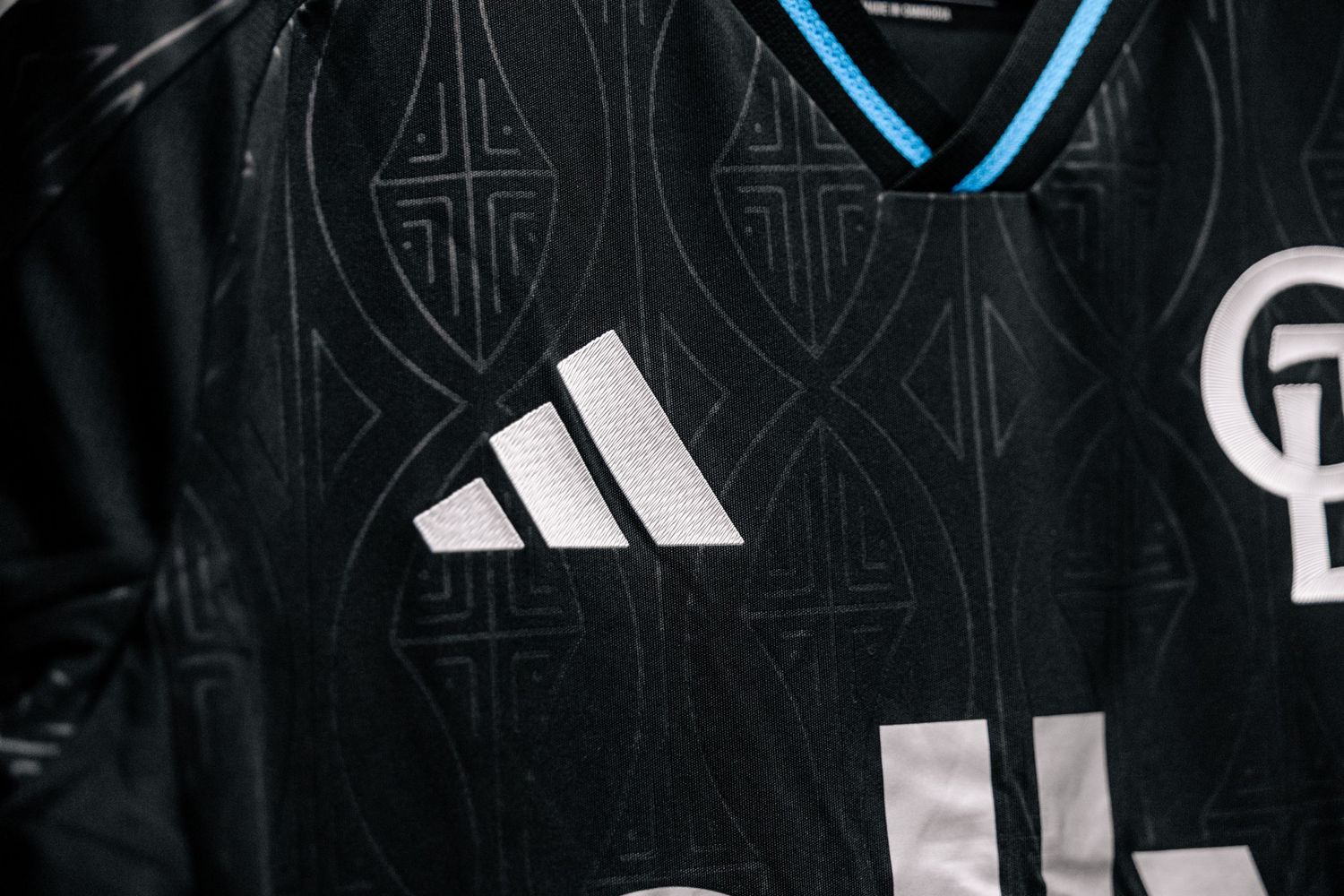Close-up of Charlotte FC black Adidas jersey featuring intricate geometric pattern with light blue collar detail.