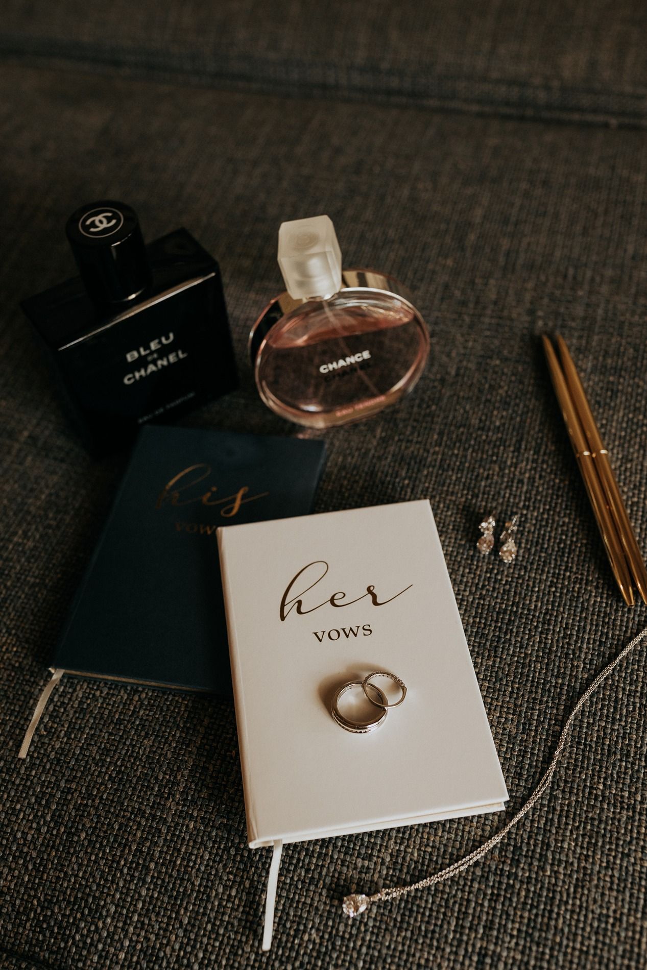 Wedding vows book and wedding rings displayed with luxury Chanel accessories on dark textured background at Rancho Bernardo Inn.