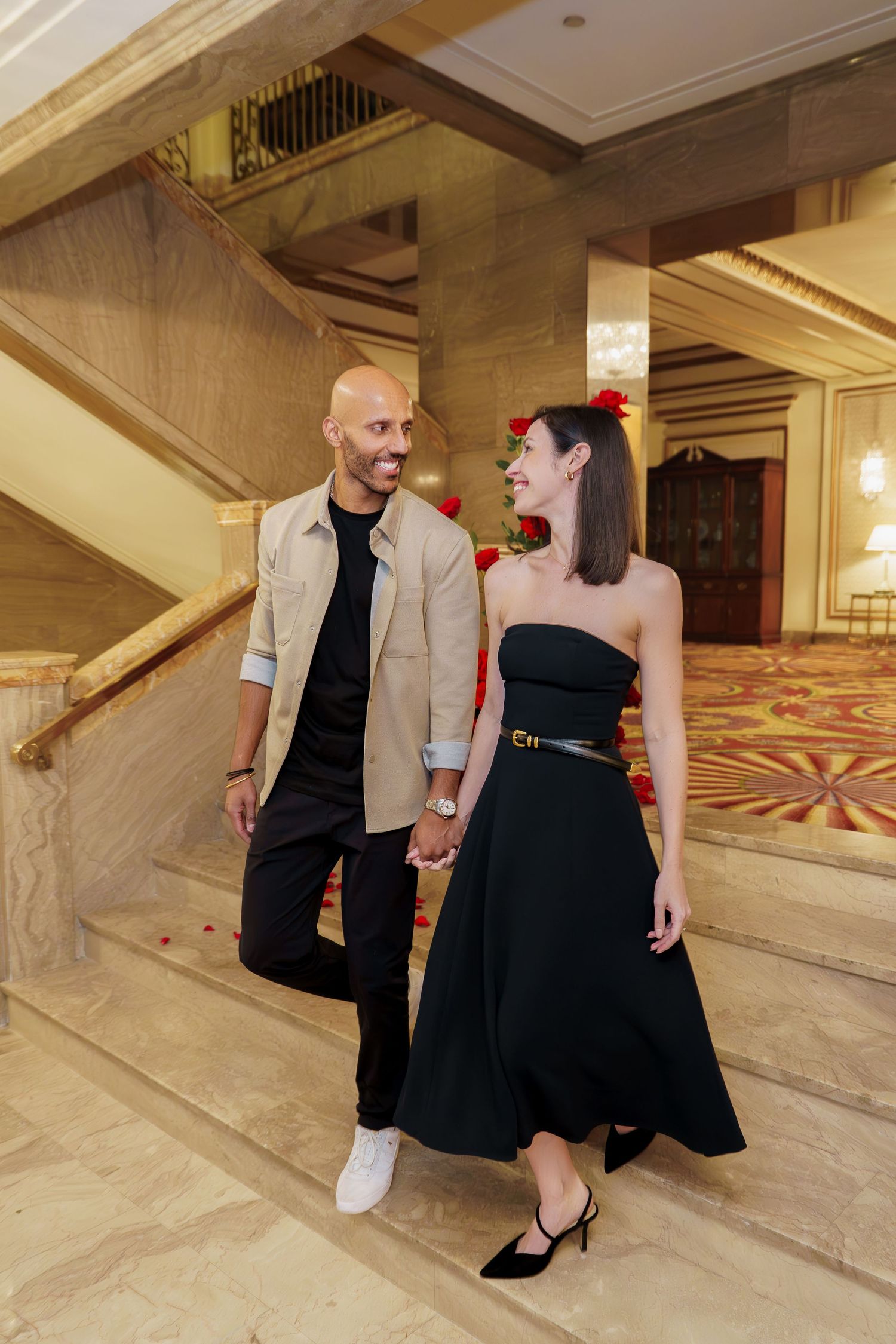 A couple in formal attire dances together in an elegant marble-floored hallway.
