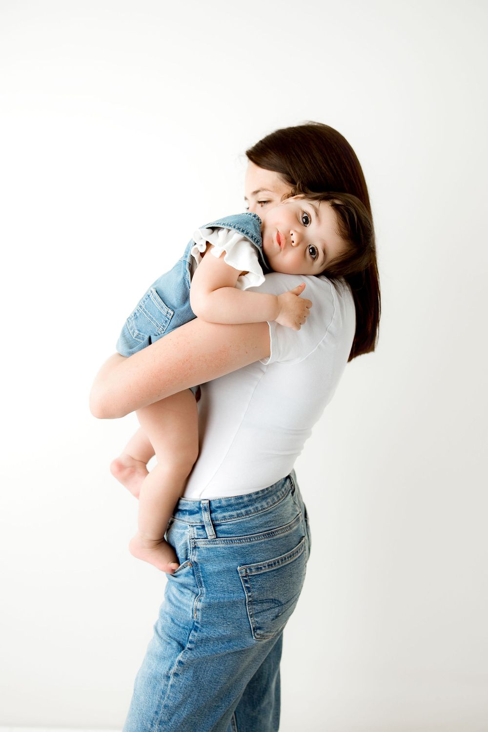 mom and baby hugging during a studio session, both are wearing jeans and white shirts
