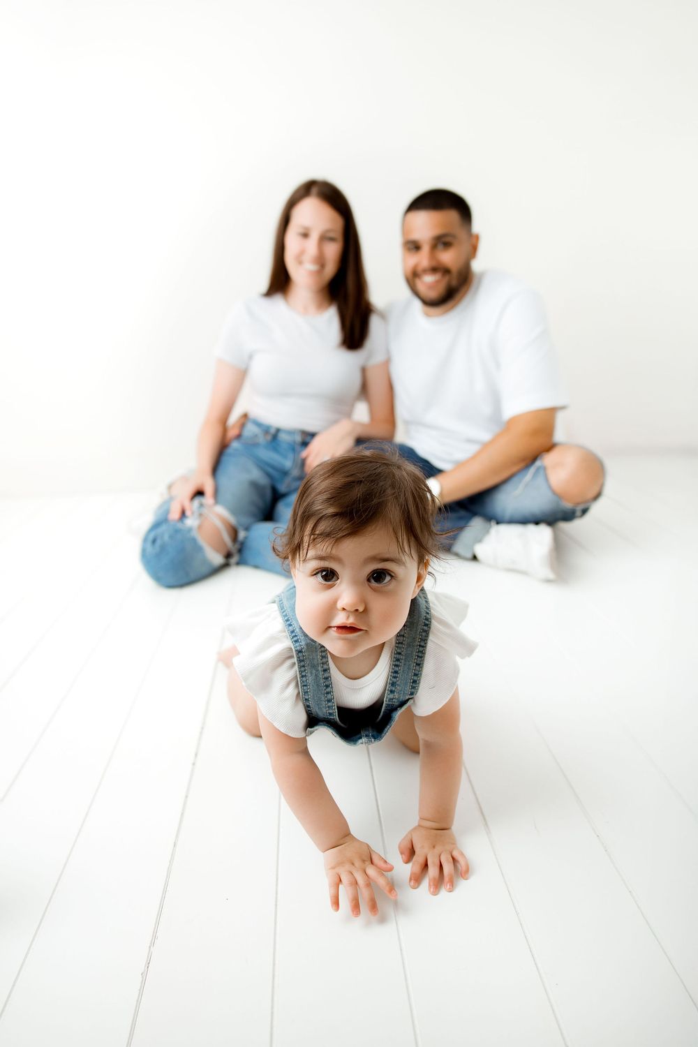 Baby crawling away from parents during a studio session in an all white set up.