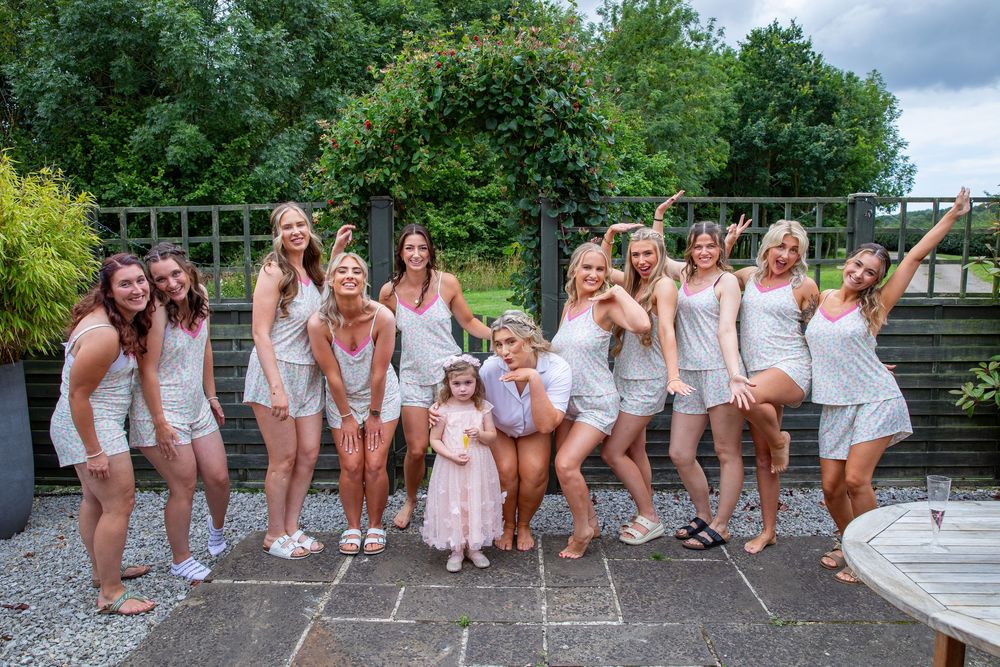 Group of bridesmaids in matching white outfits pose and celebrate together on outdoor patio during hen party.